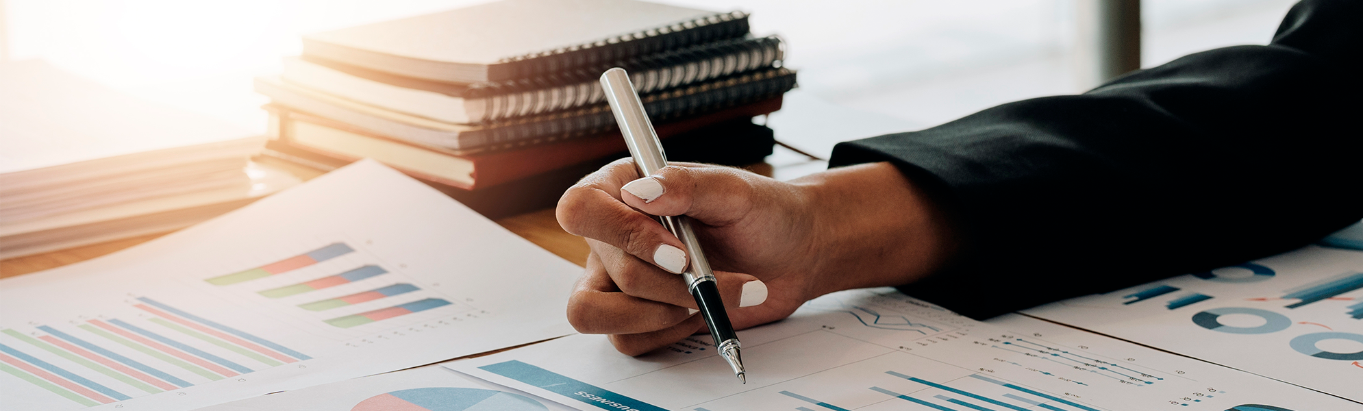 Image of a person writing with a pen next to a table with charts and management documents.